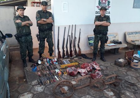 Três policiais juntos com armas, armadilhas e carne de caça