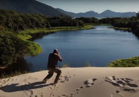 Homem fotografando sobre uma duna com um lago ao fundo