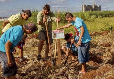 Grupo de homens cavando buraco e instalando placa em terreno com capim