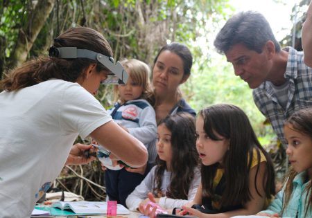 Bióloga anilhando um pássaro e crianças e adultos olhando