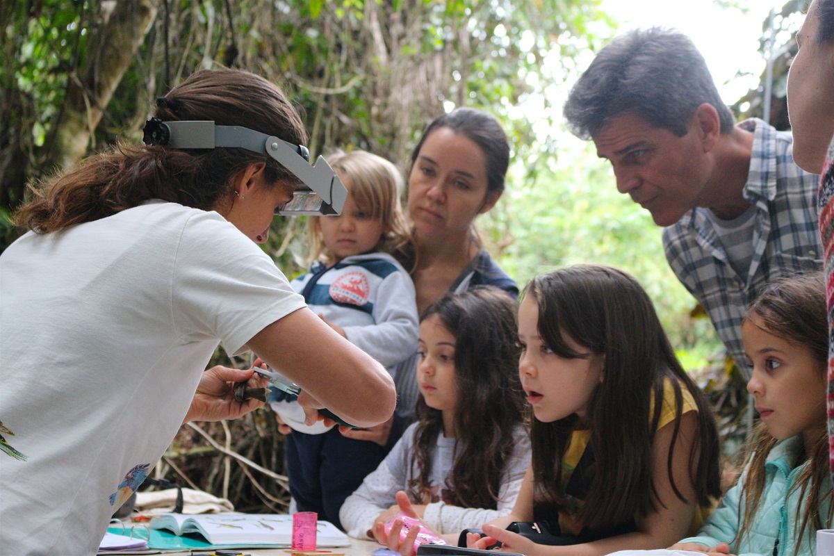 Bióloga anilhando um pássaro e crianças e adultos olhando